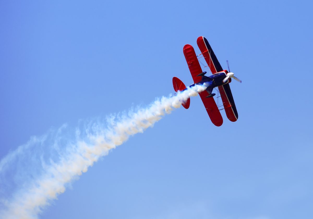 Aerial acrobatics - red propeller plane with smoke trail against clear blue sky