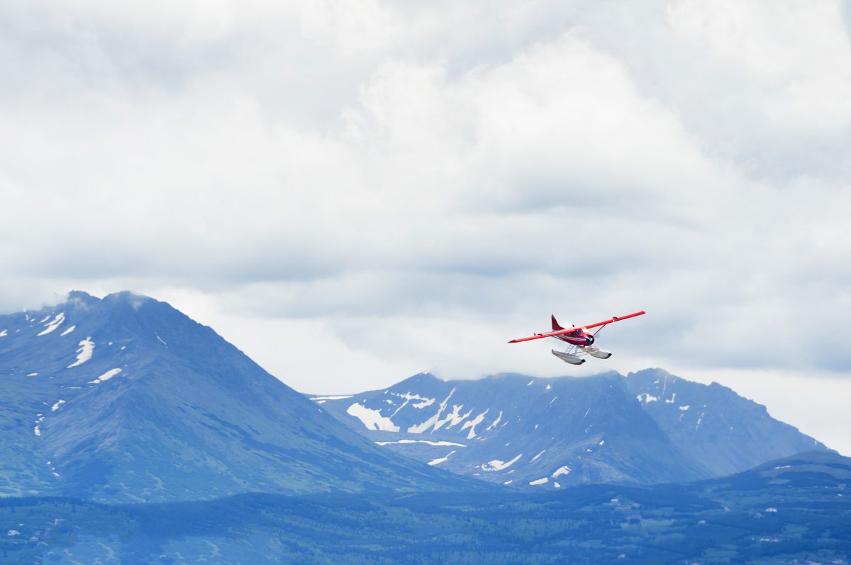 Chugach Mountain range under cloudy skies provides a majestic back drop to a seaplane as it prepares to land at Lake Hood in Anchorage, Alaska.