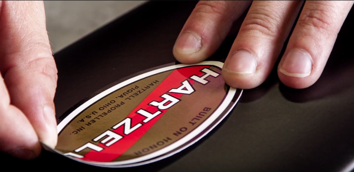 Close up of hands placing Hartzell propeller sticker on propeller blades.
